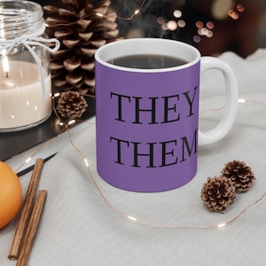 May include: Purple ceramic mug with white handle and the text "THEY THEM" in black lettering.