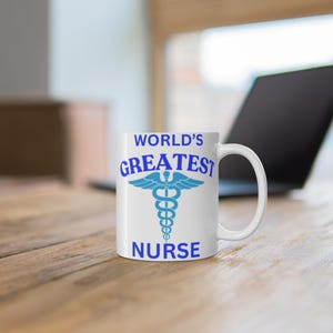 Könnte beinhalten: Eine weiße Keramiktasse mit einem blauen und weißen Caduceus-Symbol und dem Text "WORLD'S GREATEST NURSE".