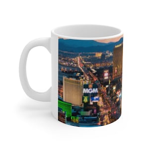 Peut inclure: Une tasse en céramique blanche avec une image colorée du ciel de Las Vegas la nuit. L'image montre les lumières de la ville et l'hôtel MGM Grand.