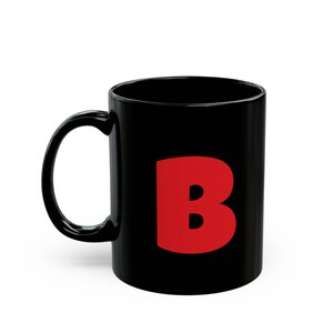 Può includere: Tazza in ceramica nera con una grande lettera rossa "B" sul davanti.