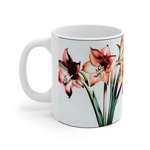 Può includere: Tazza in ceramica bianca con un design floreale colorato con fiori di amaryllis rosa, rossi e arancioni con foglie verdi.
