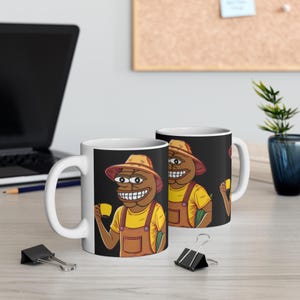 Könnte beinhalten: Weiße Keramik-Kaffeetassen mit einer Cartoon-Illustration eines lächelnden Charakters mit Strohhut, gelbem Hemd und brauner Latzhose. Die Figur hält eine gelbe Tasse. Der Hintergrund der Tasse ist schwarz.