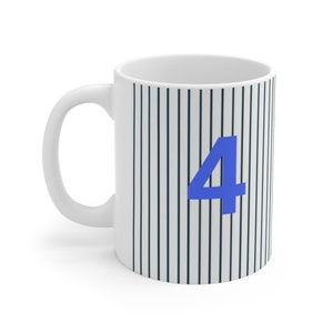 Könnte beinhalten: Weiße Keramiktasse mit einem schwarz-weißen Streifenmuster und der blauen Zahl "4" auf der Vorderseite.