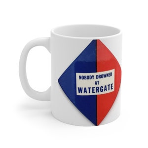 Könnte beinhalten: Weiße Keramiktasse mit einem blauen und roten rautenförmigen Design. Die Raute trägt den Text "NOBODY DROWNED AT WATERGATE" in weiß.