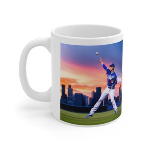 Könnte beinhalten: Weiße Keramiktasse mit einem farbenfrohen Bild eines Baseballspielers, der einen Ball vor einer Skyline einer Stadt bei Sonnenuntergang wirft. Der Spieler trägt ein blaues Trikot mit dem Wort "Dodgers" und der Nummer "42" darauf.