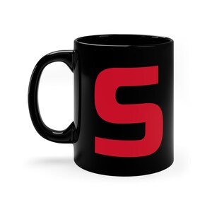 Peut inclure: Une tasse en céramique noire avec une grande lettre "S" rouge imprimée sur le devant.