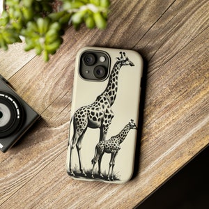 May include: A phone case with a black and white illustration of two giraffes. The larger giraffe is standing on the left side of the image, while the smaller giraffe is standing on the right side of the image. The background is a light beige color.