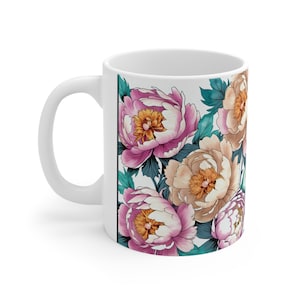 Può includere: Tazza in ceramica bianca con un design floreale con peonie rosa e beige con foglie verdi su sfondo bianco.