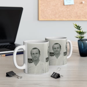 Könnte beinhalten: Zwei weiße Keramikbecher mit einem schwarz-weißen Becherdesign, das ein Männer-Fahndungsfoto zeigt. Das Fahndungsfoto hat den Text "Dallas Police" und "36398" darauf.
