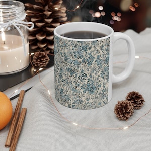 May include: A white ceramic mug with a blue and white floral pattern. The mug is filled with coffee and steam is rising from the top.