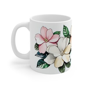 Könnte beinhalten: Weiße Keramiktasse mit einem Blumendesign mit rosa, weißen und gelben Blumen mit grünen Blättern.