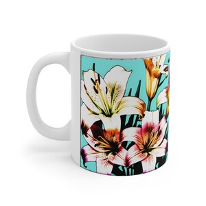 Könnte beinhalten: Weiße Keramiktasse mit einem farbenfrohen Bild von Lilien auf türkisfarbenem Hintergrund. Die Lilien sind in den Farben Weiß, Rosa, Gelb und Orange gehalten.
