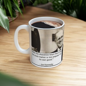 Peut inclure: Une tasse à café blanche avec une anse noire. La tasse présente une photo en noir et blanc d'un homme avec une citation : « Lorsque les cireurs de chaussures ont des pourboires, le marché boursier est trop populaire pour son propre bien. » - Joe Kennedy.