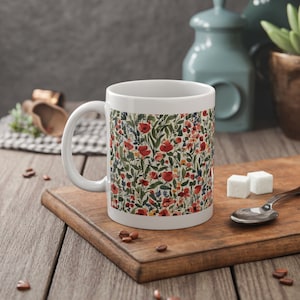 Peut inclure: Une tasse en céramique blanche avec un motif floral composé de fleurs rouges, roses et bleues sur un fond vert. La tasse a une anse blanche.