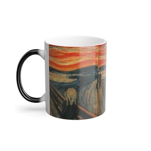 Peut inclure: Une tasse à café en céramique blanche avec une poignée noire. La tasse présente une image couleur de la peinture "Le Cri" d'Edvard Munch. L'image est imprimée des deux côtés de la tasse.