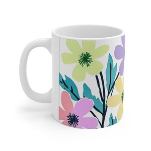 Könnte beinhalten: Weiße Keramiktasse mit einem Blumenmuster. Das Design zeigt rosa, gelbe und lila Blumen mit grünen Blättern auf weißem Hintergrund.