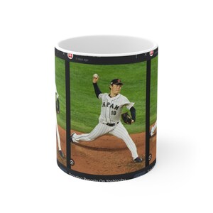 Könnte beinhalten: Ein Baseball-Pitcher in einer weißen und blauen Uniform mit dem Wort "JAPAN" und der Nummer "18" auf dem Rücken wirft einen Pitch auf einem Baseballfeld. Der Pitcher trägt eine weiße Kappe mit einem roten Logo.