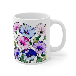 Könnte beinhalten: Weiße Keramiktasse mit einem bunten Blumenmuster. Das Design zeigt rosa, blaue und lila Blumen mit grünen Blättern.