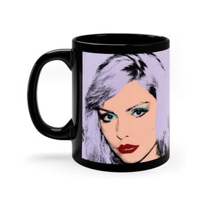 Peut inclure: Mug en céramique noire avec une anse blanche. Le mug présente une image colorée de style pop art d'une femme aux cheveux violets et au fard à paupières bleu.