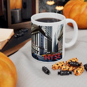 Peut inclure: Une tasse en céramique blanche avec une anse noire. La tasse présente une image colorée du bâtiment de la Bourse de New York avec le texte "NYSE" en rouge. La tasse est remplie de café et de la vapeur s'élève du haut.