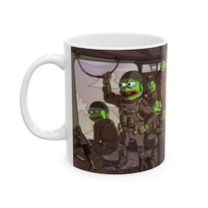 Peut inclure: Une tasse en céramique blanche avec une illustration colorée de grenouilles de dessin animé vertes habillées en soldats dans un hélicoptère. Les grenouilles tiennent des armes et portent des casques. L'arrière-plan est une représentation de dessin animé d'un ciel avec des nuages.