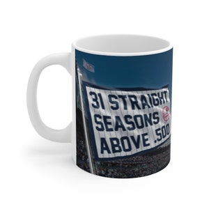 Könnte beinhalten: Weiße Keramik-Kaffeetasse mit einem Foto eines Baseballstadions. Das Foto zeigt ein großes Banner mit der Aufschrift "31 Straight Seasons Above .500".