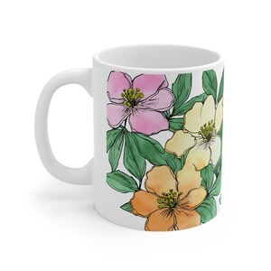 Könnte beinhalten: Weiße Keramiktasse mit einem Blumendesign. Das Design zeigt rosa, gelbe und orangefarbene Blumen mit grünen Blättern.