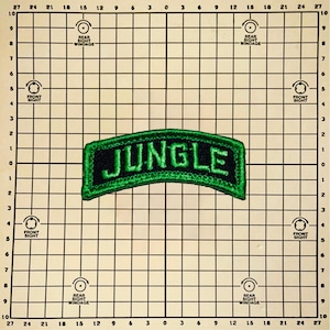 May include: A black and green embroidered patch with the word "JUNGLE" in green lettering. The patch has a curved shape and is set against a grid background.