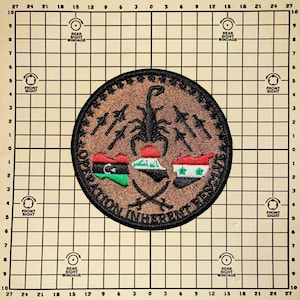 May include: A brown, circular patch with a scorpion design and the text "Operation Inherent Resolve" around the edge. The scorpion is surrounded by three flags: the flag of Libya, the flag of Iraq, and the flag of Syria.