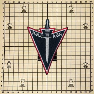 May include: A black, navy, and red patch with the text "RSLC ABN" and a sword design. The patch is in a triangular shape with a red border. The background is a grid pattern with text and circles.