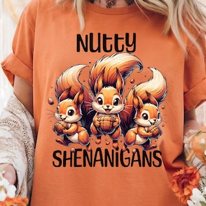 May include: Orange t-shirt featuring a graphic of three squirrels holding nuts and the text "Nutty Shenanigans".