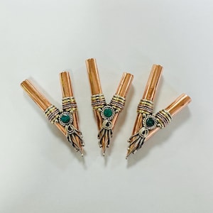 May include: Five copper-colored metal pipes with decorative silver and gold bands. Each pipe features a central green stone and ornate silver detailing at the base. The pipes are arranged on a white surface.