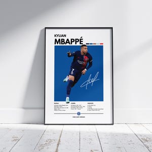 Pode incluir: Pôster emoldurado com Kylian Mbappé em uniforme de futebol azul marinho sobre um fundo azul. O pôster inclui seu nome, assinatura e detalhes da carreira. A moldura é preta e o pôster é exibido em uma parede branca.