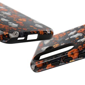 May include: Black phone case with a Halloween-themed pattern. The case features white ghosts, orange pumpkins, and floral accents on a dark background. The case has a black border and cutouts for the phone's features.