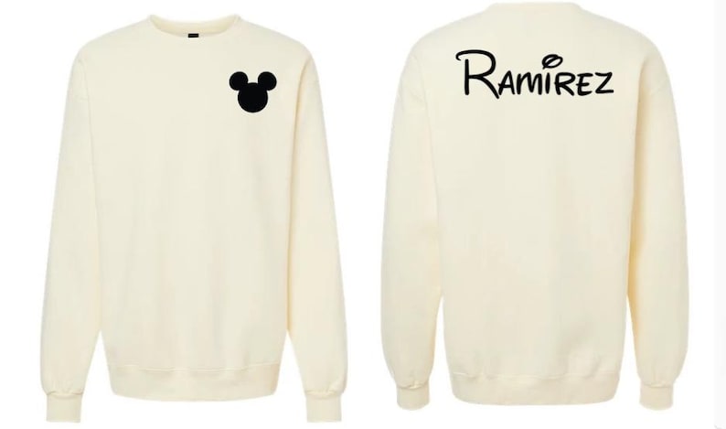 May include: A cream-colored crewneck sweatshirt featuring a black silhouette of a mouse head on the left chest and the text "Ramirez" in a stylized black font across the upper back. The garment has long sleeves and a ribbed collar, cuffs, and hem.