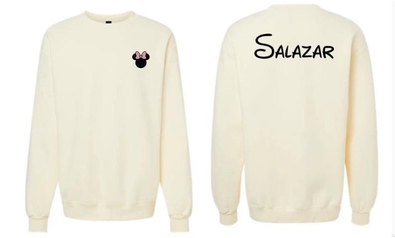 May include: A cream-colored long-sleeve sweatshirt featuring a small black Minnie Mouse head icon with a pink bow on the front left chest and the name Salazar printed in a black stylized script font across the upper back of the garment.