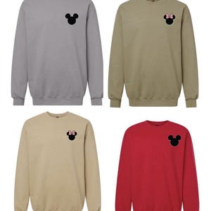 May include: Four crewneck sweatshirts in gray, tan, beige, and red. Each features a small, centered chest graphic of a black mouse silhouette. Two of the silhouettes include a small pink bow detail on the head, while two remain plain black.