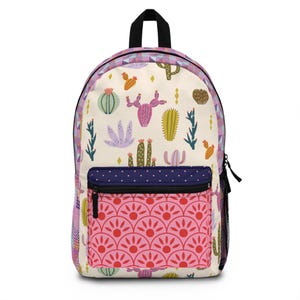 May include: A backpack with a cream-colored background featuring a cactus pattern in various colors. The front pocket has a pink floral design. The top handle and zipper are black. The backpack has a side mesh pocket.
