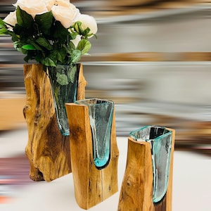 May include: Three decorative vases. Each vase features a clear glass insert within a natural wood base. The vase on the left holds white roses. The wood bases have a natural, rustic appearance, with visible grain and knots.