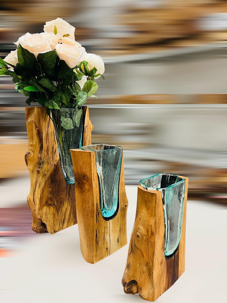 May include: Three decorative vases. Each vase features a clear glass insert within a natural wood base. The vase on the left holds white roses. The wood bases have a natural, rustic appearance, with visible grain and knots.