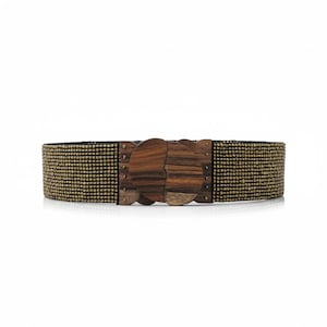 Pode incluir: Cinto largo com design de contas douradas e pretas. A fivela decorativa de madeira apresenta um design &uacute;nico e interligado. A fivela &eacute; feita de madeira escura com padr&otilde;es de gr&atilde;o vis&iacute;veis. Acess&oacute;rio de moda.