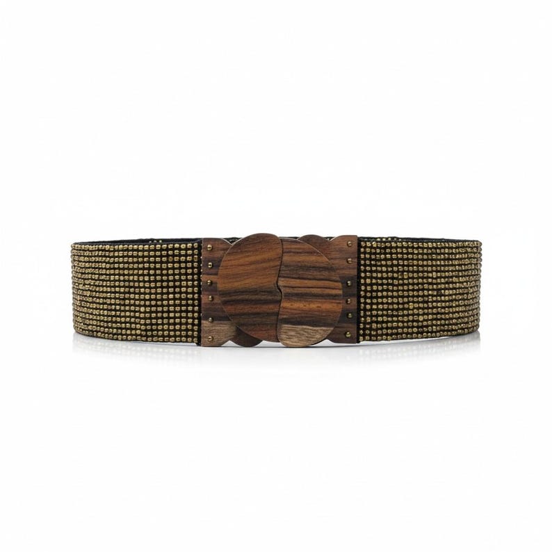 Pode incluir: Cinto largo com design de contas douradas e pretas. A fivela decorativa de madeira apresenta um design &uacute;nico e interligado. A fivela &eacute; feita de madeira escura com padr&otilde;es de gr&atilde;o vis&iacute;veis. Acess&oacute;rio de moda.