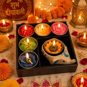 May include: A black partitioned box containing five flower-shaped candles in red, yellow, pink, green, and blue, plus one yellow sunflower candle held in a ceramic elephant-shaped holder. Each candle features a lit wick, creating a warm glow.