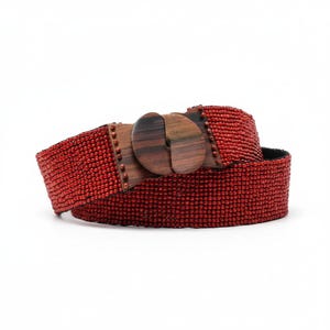 Pode incluir: Um cinto vermelho com contas e fivela de madeira. O cinto &eacute; feito de pequenas contas vermelhas muito juntas. A fivela &eacute; de madeira escura com um design circular. O cinto tem aproximadamente 5 cm de largura.