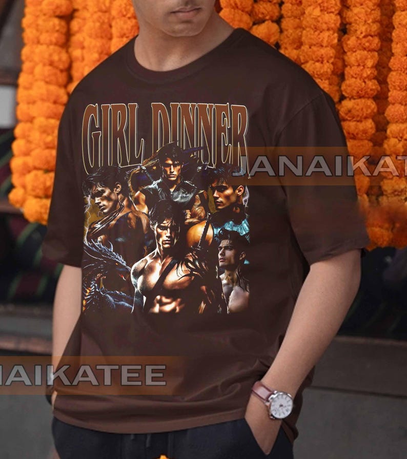 May include: Brown t-shirt with the text "GIRL DINNER" in a vintage style font. The shirt features a collage of muscular male figures. The shirt is a crew neck and has short sleeves.