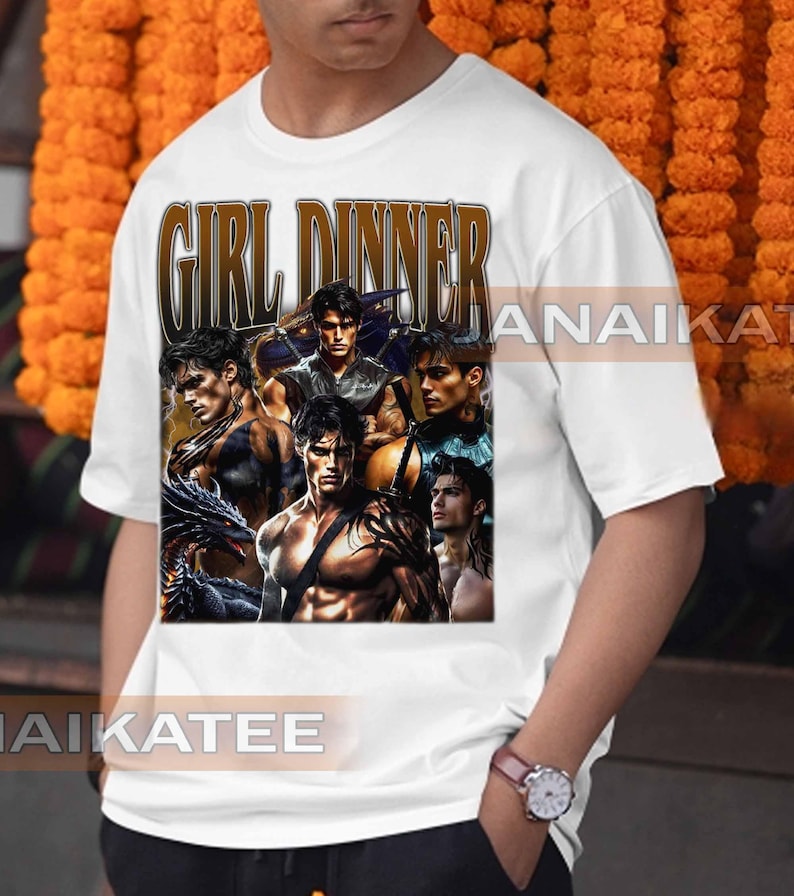 May include: White t-shirt featuring a graphic design with the text "GIRL DINNER" in a brown, vintage-style font. The graphic includes multiple images of muscular men. The shirt is a casual, short-sleeved style.