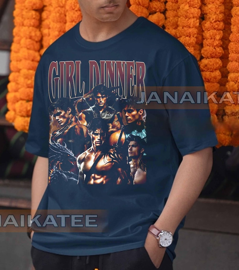 May include: Navy blue t-shirt with the text "GIRL DINNER" in a vintage style. The shirt features a collage of muscular men in various poses. The overall design has a retro aesthetic.
