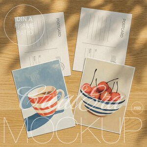 Könnte beinhalten: Vier Postkarten auf einer Holzoberfläche. Zwei Karten sind leer mit dem Aufdruck "POSTCARD". Die anderen beiden zeigen Illustrationen: eine Tasse mit rot-weißen Streifen und eine Schüssel mit Kirschen. Das Wort "MOCKUP" ist sichtbar.