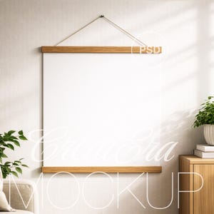 May include: A blank white poster hanging on a wall with wooden bars at the top and bottom. The poster is suspended by a natural-colored cord. The background includes a neutral-toned wall, a wooden cabinet, and a potted plant.
