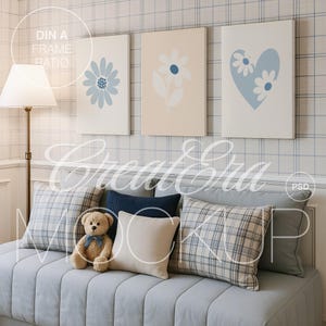 Op de afbeelding: Een gezellige woonkamer met een lichtblauwe bank versierd met kussens in verschillende patronen. Boven de bank hangen drie ingelijste bloemenkunstwerken aan de muur. Een teddybeer zit op de bank. Een staande lamp staat links.